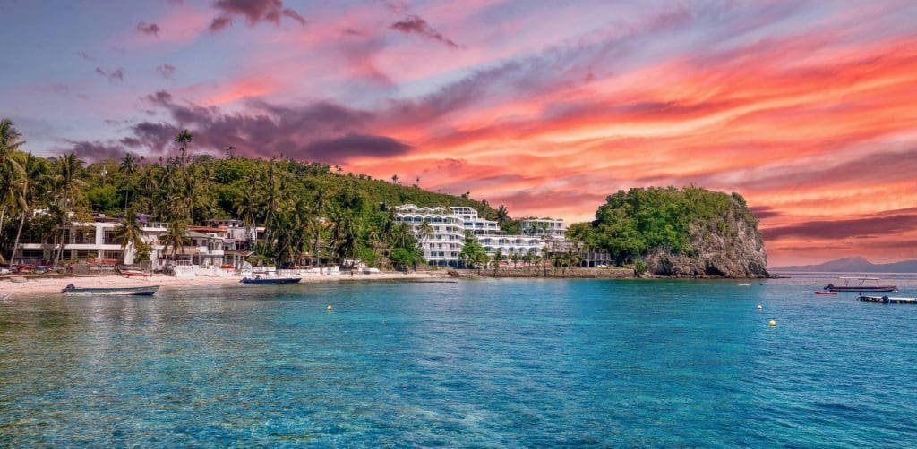 Amazing sunset over Puerto Galera with vibrant orange and pink skies reflecting on calm ocean waters.